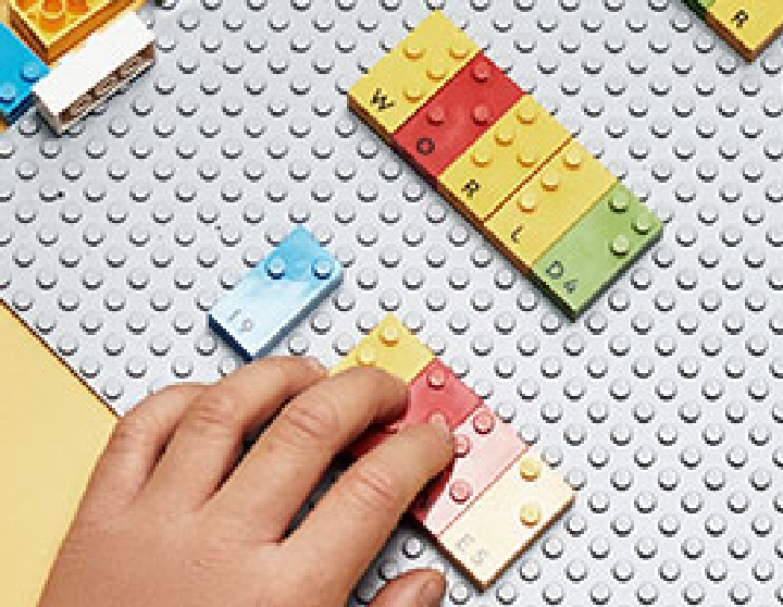 LEGO Braille bricks on a gray base plate, along with a kids hand